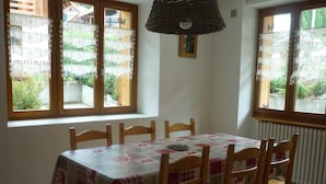 A dining area with a table set for four, wooden chairs, lace curtains, and a hanging light fixture.
