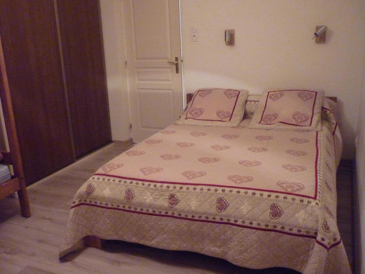 A bedroom with a bed covered in a patterned bedspread, a wooden wardrobe, and a door.