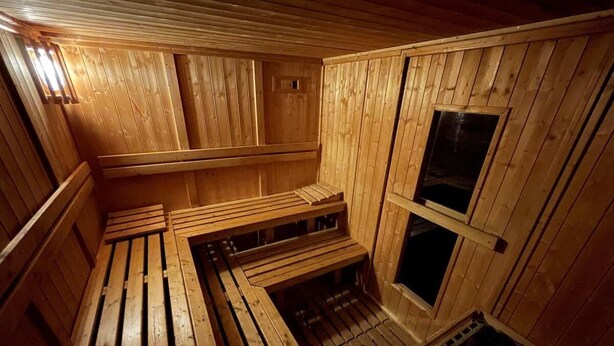 A sauna with wooden benches and a sloped floor, wooden walls, and a window.