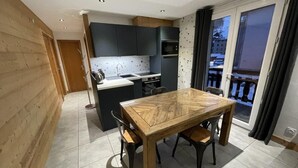 A modern kitchen with dark cabinets, a wooden dining table, and a view of the outside through a sliding glass door.