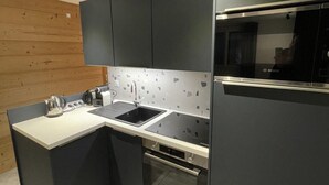 A modern kitchen with dark cabinetry, a stainless steel refrigerator, a built-in oven, and a countertop with a kettle.