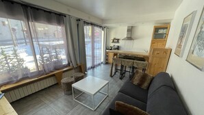 Ett modernt vardagsrum med en soffa, ett soffbord och en matplats, med ett kök synligt i bakgrunden.