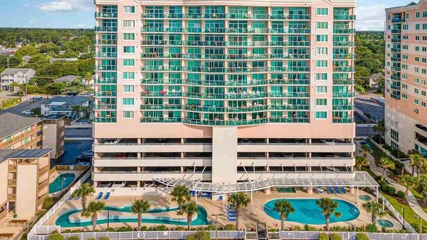 A multi-story hotel with a central courtyard featuring a swimming pool and palm trees. - Luxury Penthouse 4BR Condo - Great for Families! (North Myrtle Beach)