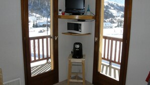 A corner room with a TV, microwave, and coffee maker on a shelf, overlooking a snowy mountain.