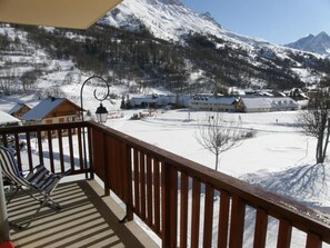 Un paysage enneigé avec une terrasse en bois et une chaise, d’où l’on peut admirer un village et des montagnes.