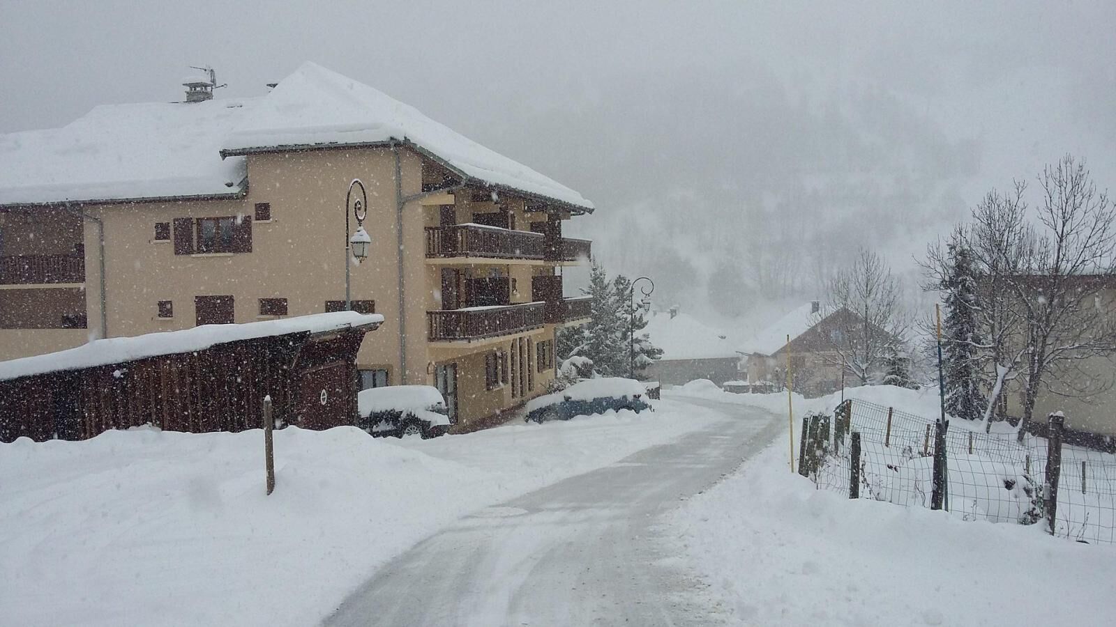 A snow-covered building with multiple balconies, a visible entrance, and a snow-covered road leading to it.