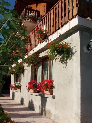 Een gebouw met een balkon, versierd met rode bloemen, een betonnen gevel en een houten hekwerk.