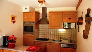 A compact kitchen with wooden cabinets, a built-in oven, a microwave, and a gas stove. - 1st floor, terrace, ski locker, 30m², Valloire (Valloire)
