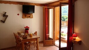 A dining area with a wooden table, chairs, a television mounted on the wall, and a view of a balcony with red curtains. - 1st floor, terrace, ski locker, 30m², Valloire (Valloire)