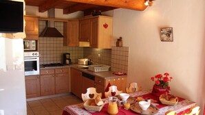 Uma cozinha com armários de madeira, painel de azulejos e um espaço de jantar com toalha vermelha e cadeiras em formato de coração.