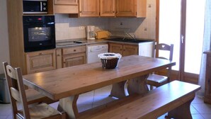 Uma cozinha com armários de madeira, forno embutido e uma mesa de jantar com cadeiras.