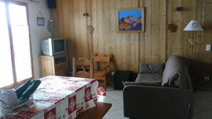 Ein Zimmer mit Holzwänden, einem Fernseher, einem Sofa, einem Tisch mit Tischdecke und einem Gemälde an der Wand.