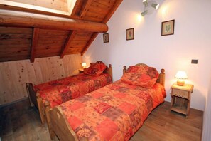 A room with two wooden beds, each with a headboard, a wooden floor, and a sloped ceiling with wooden beams. There are two bedside tables with lamps. - 300m from ski slopes, 2nd floor, terrace, parking, ski locker, 40m², Valloire (Valloire)