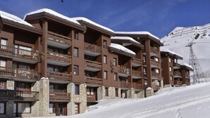 Ein mehrstöckiges Hotel mit Balkonen und Steinsäulen, umgeben von Schnee und einer Skipiste.