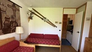 Ein kompakter Raum mit zwei Holzbetten, einer kleinen Küchenzeile und einer Tür zu einem weiteren Zimmer.