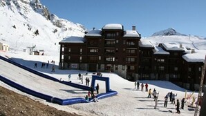 Ein Skigebiet mit Seilbahn, einem mehrstöckigen Gebäude und einem verschneiten Berg im Hintergrund.