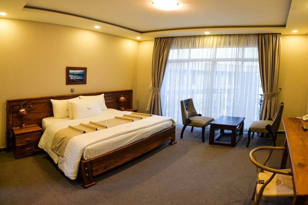 Une chambre d’hôtel avec un grand lit, deux chaises, une petite table, un bureau, une télévision et un ventilateur.