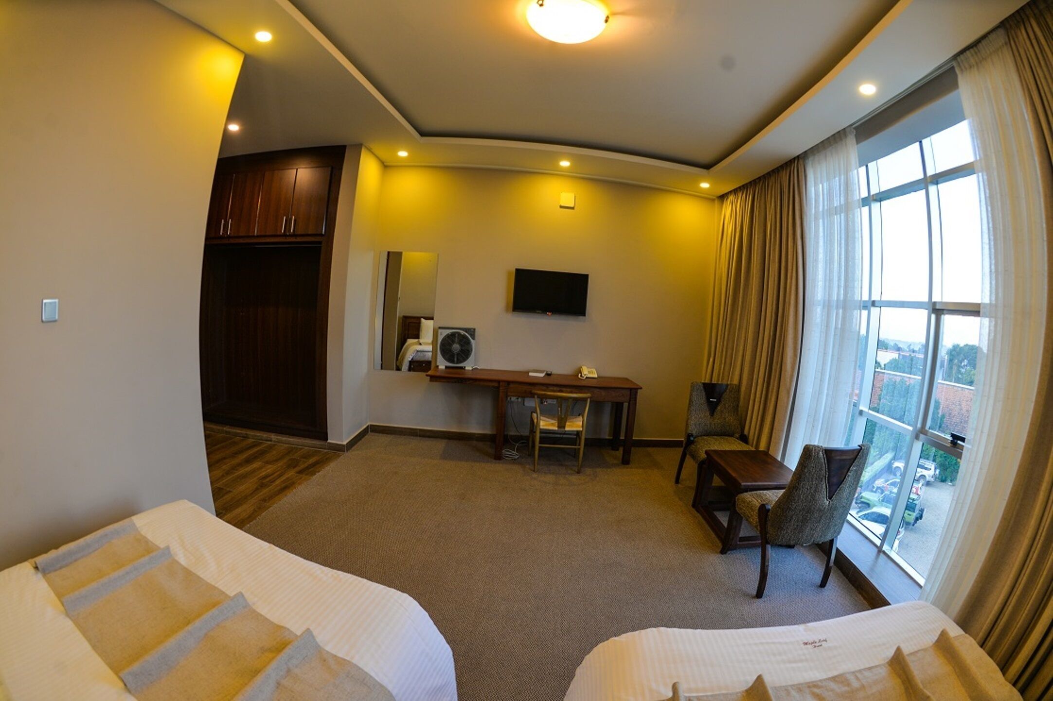 Habitación de hotel con dos camas, un escritorio, una silla, un televisor y un ventanal con cortinas.