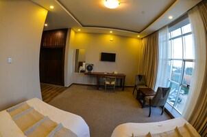Habitación de hotel con dos camas, un escritorio, una silla, un televisor y un ventanal con cortinas.