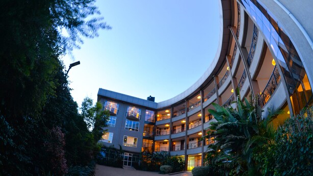 A multi-story hotel with a curved facade, multiple balconies, and a landscaped courtyard. - Maple Leaf Hotel (Masaka)