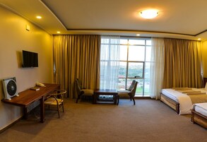 Una habitación de hotel con cama, un escritorio con silla, televisión y un ventanal con cortinas.