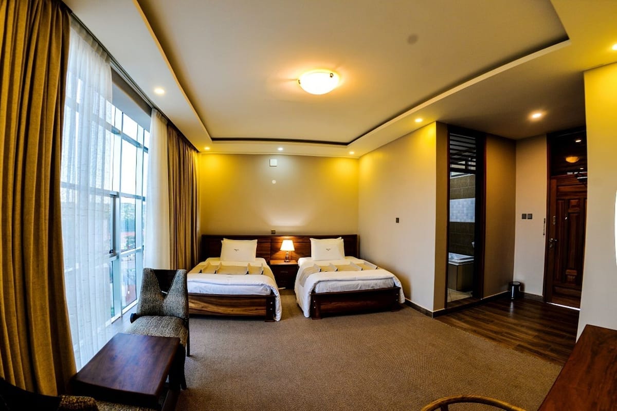 Une chambre d’hôtel avec deux lits, un bureau, une chaise et une fenêtre avec des rideaux.