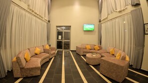 A spacious lobby with a curved sofa set, a coffee table, and a flat-screen TV mounted on the wall. - Maple Leaf Hotel (Masaka)