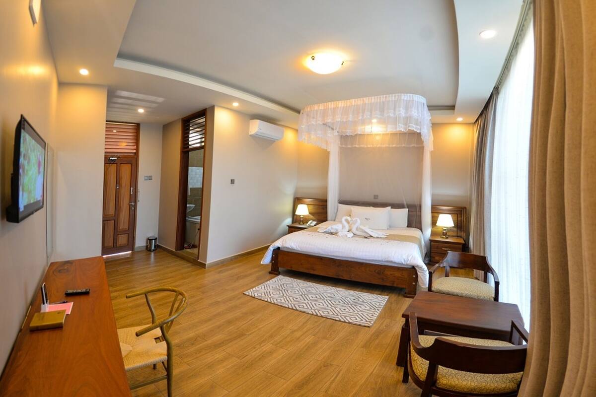 Une chambre d’hôtel comprenant un lit, des tables de chevet, un bureau, une chaise, un tapis à motifs et une fenêtre avec des rideaux.