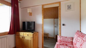 Una habitación con un armario de madera, televisor, sofá rojo estampado y techo de madera.