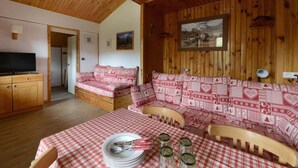 Una habitación acogedora con paredes de madera y un mantel a cuadros. Hay un sofá con cojines con estampado de corazones y un televisor sobre un mueble de madera.