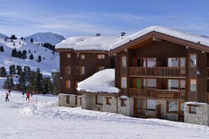 A wooden lodge with a stone foundation, multiple balconies, and a snow-covered roof. - 100m from resort center, view ski slopes/ski slopes, tv, ski locker, 35m², La Plagne (La Plagne)