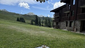 Ein Gebäude mit einer Stein-Fassade und hölzernen Balkonen, vor einer grünen Wiese und fernen Bergen gelegen.