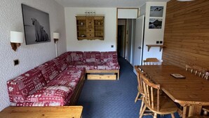 Ein gemütliches Zimmer mit einem rot-weißen Sofas, einem Holzesstisch mit Stühlen und einem blauen Teppich.