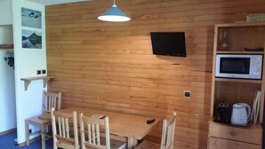Ein Zimmer mit Holzvertäfelung, ausgestattet mit einem Tisch, Stühlen, einem Wand-Fernseher und einer Mikrowelle auf einem Regal.