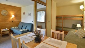 Ein gemütliches Zimmer mit Holzboden, einem blauen Sofa, einem Holztisch mit Papieren und einem Etagenbett mit Lampe.