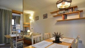 Ein gemütliches Zimmer mit einem Etagenbett, einem Esstisch mit Unterlagen, einer Lampe und einem Bücherregal.