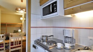 Eine kompakte Küche mit Mikrowelle, Kaffeemaschine und Herd. Ein Essbereich mit Tisch und Stühlen ist vorhanden.