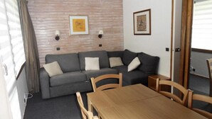 A compact living space with a sofa, a wooden dining table, and two wall-mounted lamps. - 50m from resort center, Ground floor, tv, ski locker, 28m², La Plagne (La Plagne)