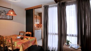 A dining area with a table set for two, a kitchen in the background, and a window with curtains. - 50m from resort center, Ground floor, tv, ski locker, 28m², La Plagne (La Plagne)