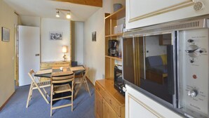 Una habitación acogedora con una mesa de comedor de madera, sillas, una kitchenette con estufa y una cama con manta azul a cuadros.