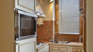 Una cocina compacta con horno empotrado, un lavamanos y una ventana con persianas.