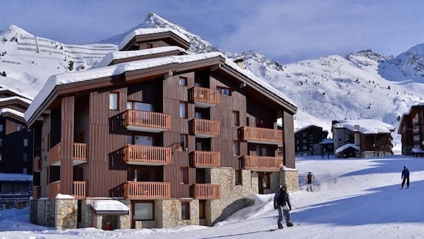 Un edificio de madera de varios pisos con balcones, rodeado de montañas nevadas.
