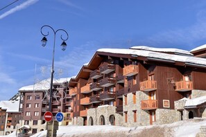 A multi-story hotel with stone and wooden balconies, a ski slope in the background, and a clear blue sky. - 100m from ski slopes, 3rd floor, view ski slopes, balcony, tv, 33m², La Plagne (La Plagne)