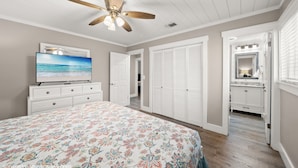 A bedroom with a bed, a ceiling fan, a TV, a walk-in closet, and a bathroom with a vanity and mirror. - Fam & Pet Friendly, PVT Heated Pool Steps 2 Beach (Panama City Beach)