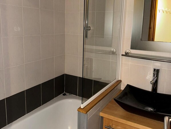 A modern bathroom with a glass-enclosed shower, a white bathtub, and a black sink with a wooden countertop.