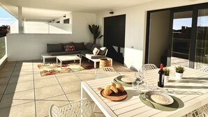 En balkon med et spisebord dækket til to personer, en sofa og en potteplante.
