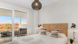 Et moderne soveværelse med en stor seng, to sengeborde, en rattan sengegavl og udsigt til bygninger gennem en skydedør.