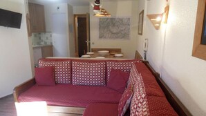A cozy living room with a red sofa, a dining table with plates, and a kitchen in the background. - 100m from resort center, 6th floor, view ski slopes, balcony, tv, 40m², La Plagne (La Plagne)