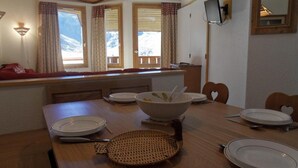 A dining area with a wooden table set for four, a large bowl, and a woven placemat. - 100m from resort center, 6th floor, view ski slopes, balcony, tv, 40m², La Plagne (La Plagne)