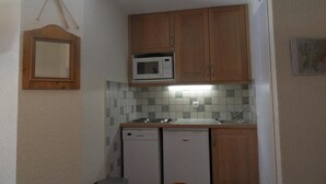 A compact kitchen with wooden cabinets, a microwave, a dishwasher, and a tiled backsplash. - 100m from resort center, 6th floor, view ski slopes, balcony, tv, 40m², La Plagne (La Plagne)